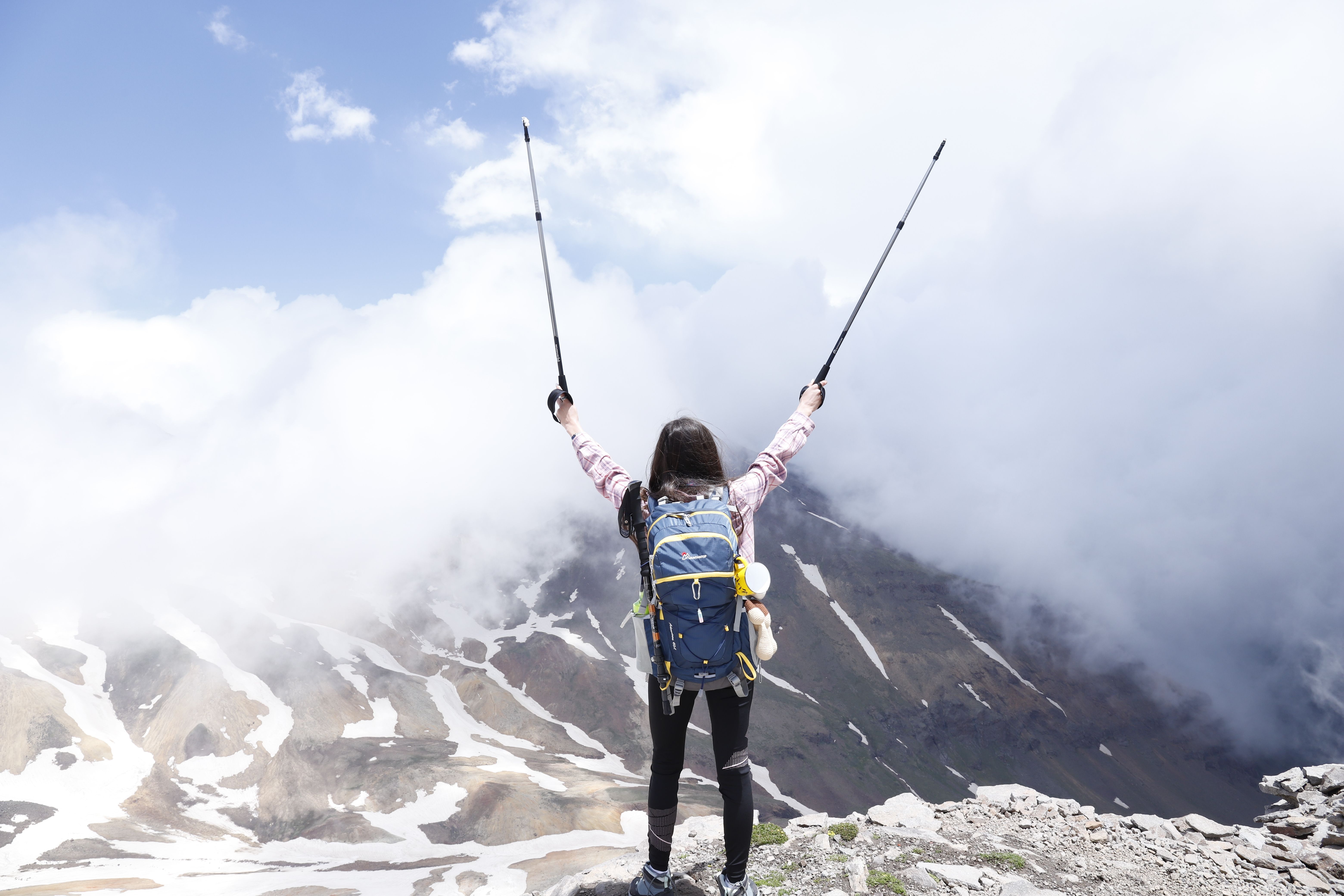 Woman with a backpack celebrating reaching a mountain summit, valuing experiences over possessions