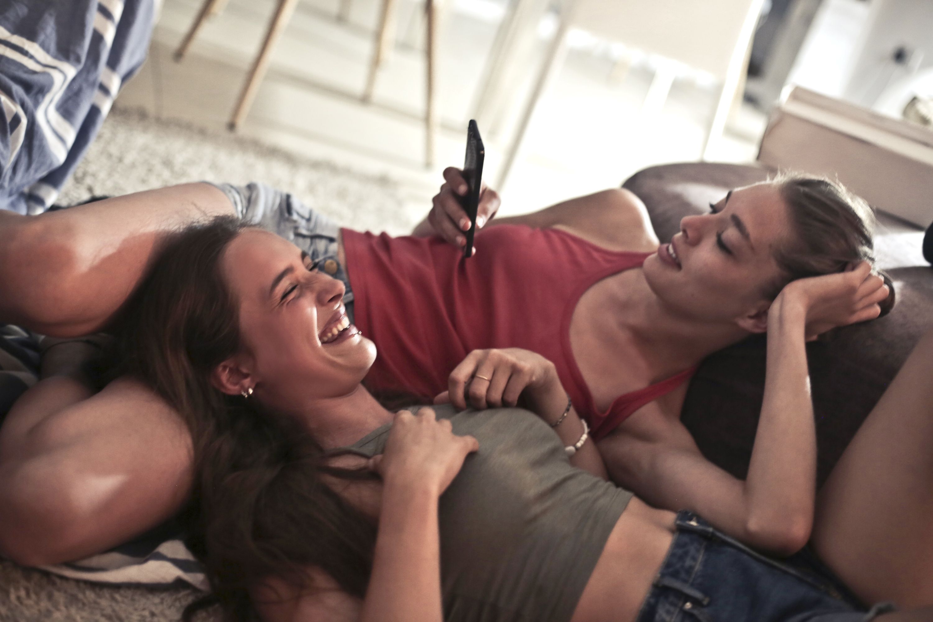 Two young women laughing together indoors in a warm, relaxed moment of genuine friendship