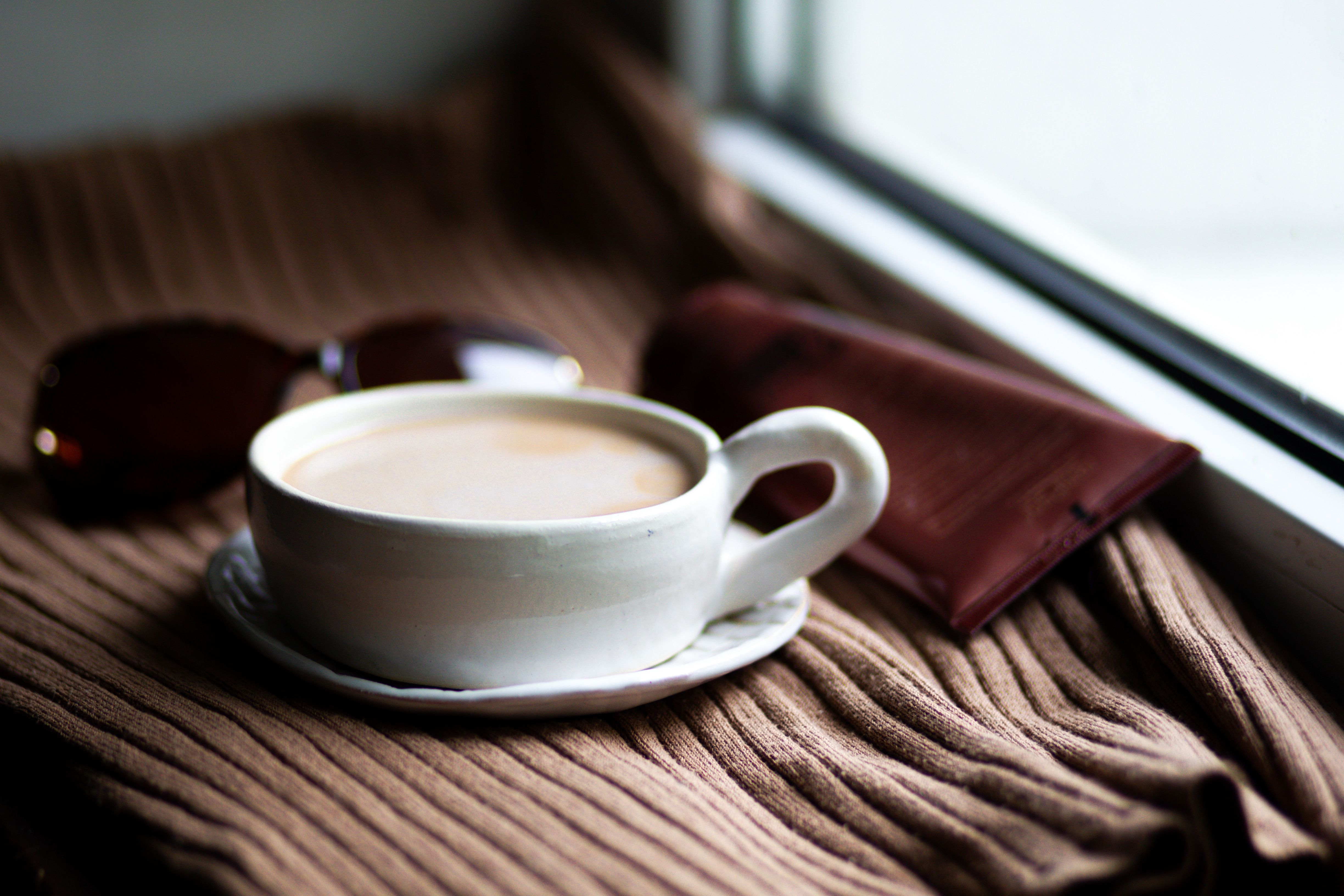 Warm coffee cup resting on a blanket by a bright window in a cozy home