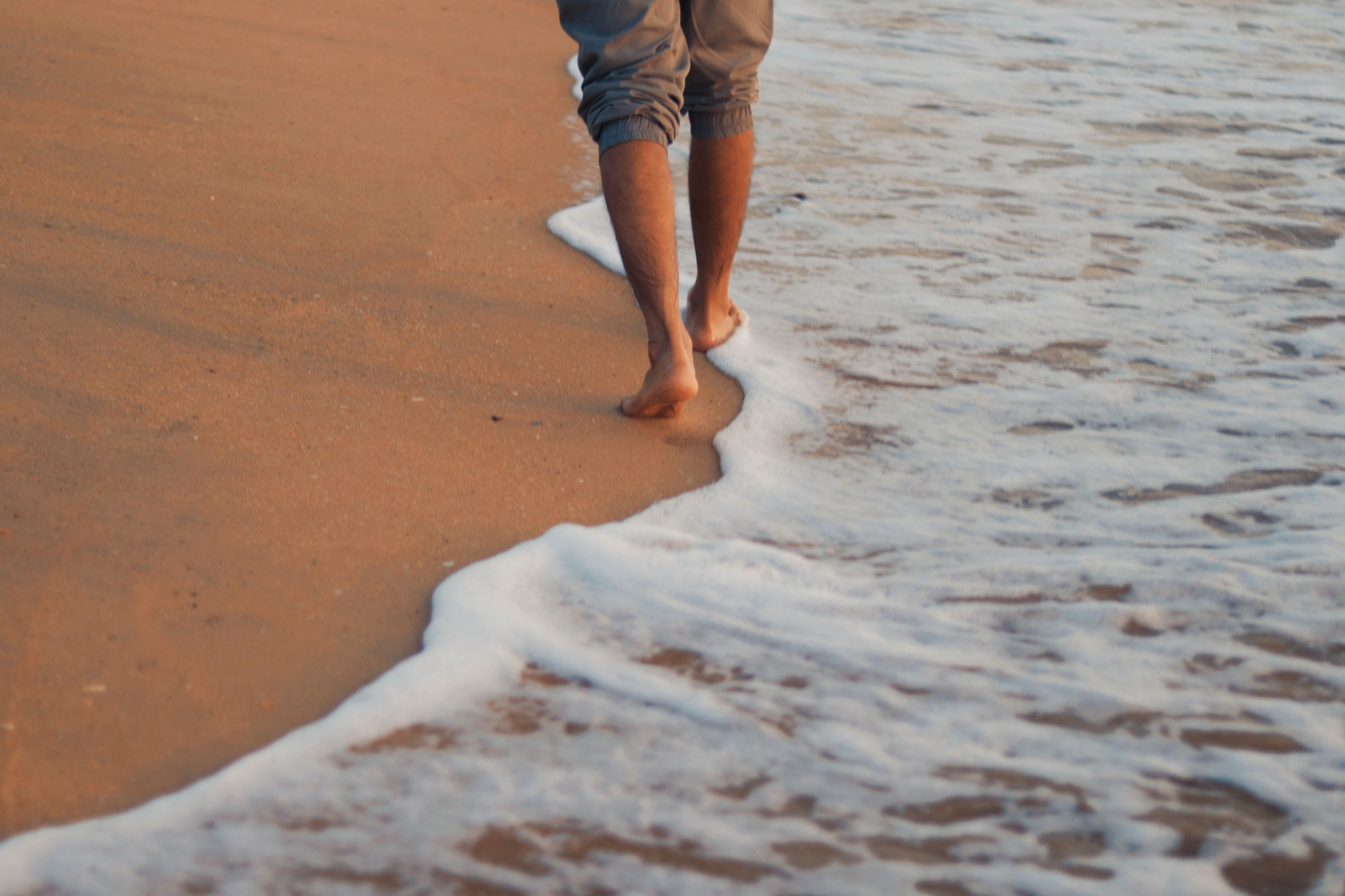 Person walking barefoot along a sandy beach at sunrise with gentle waves, a simple moment of wellbeing